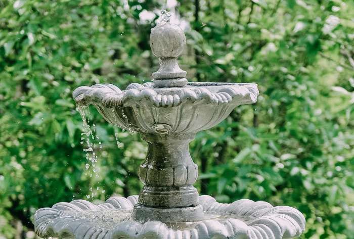 Tiered stone garden fountain with water flowing over carved basin in a landscaped outdoor setting