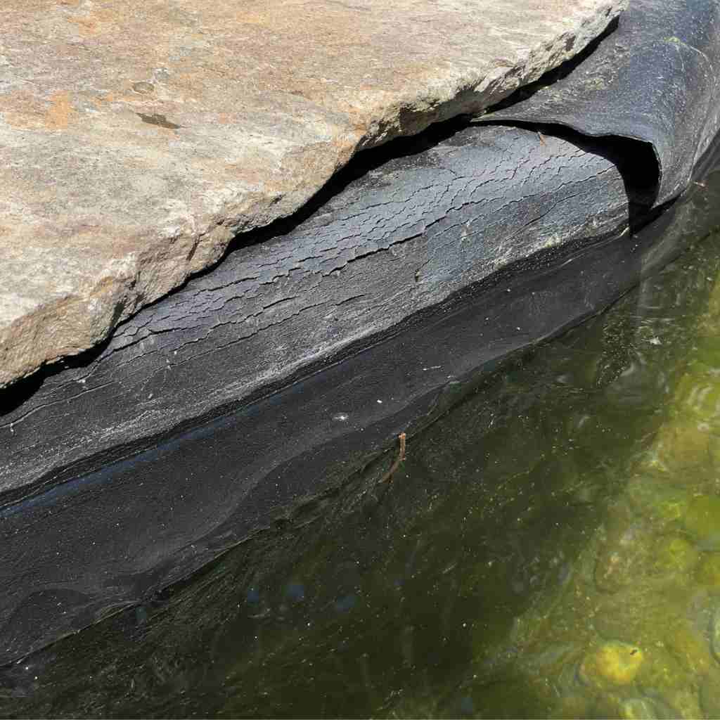 EPDM pond liner showing UV degradation with cracking and stiffness above the waterline contrasted with smooth flexible liner below the waterline